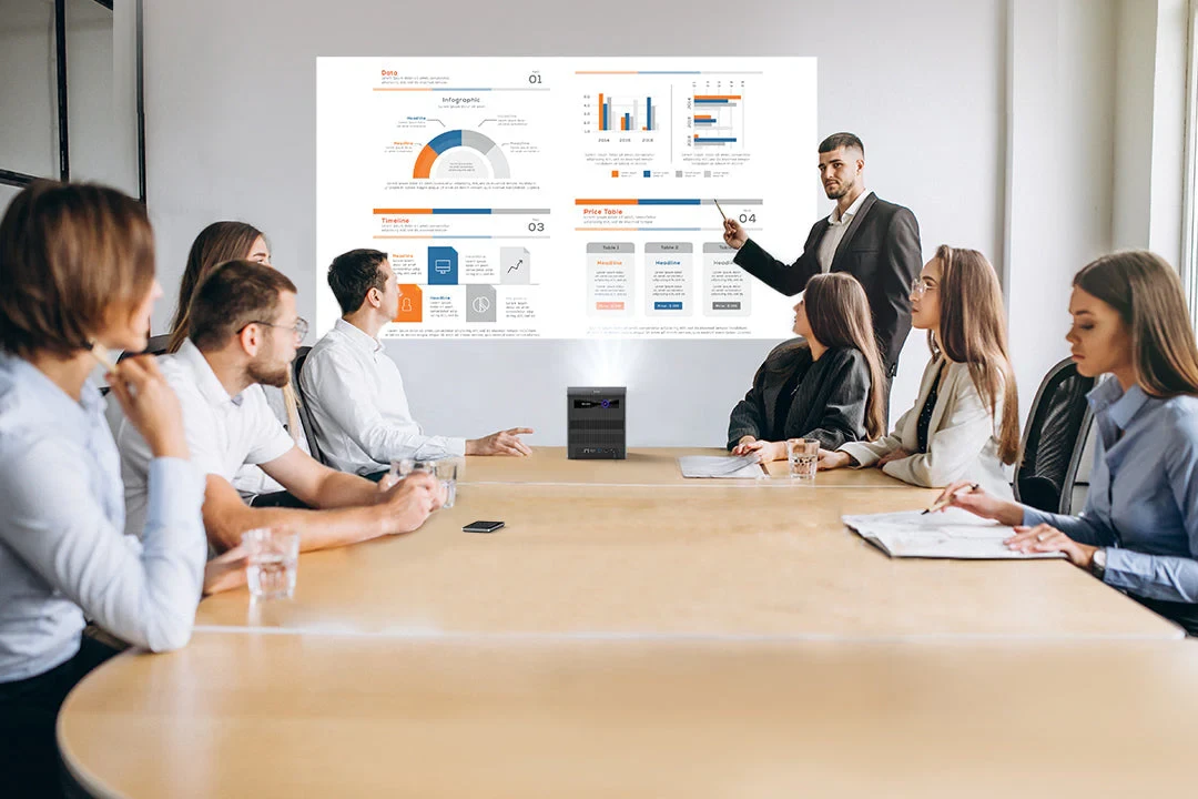 A man stands by a screen presenting charts and graphs to six seated colleagues in a meeting room.