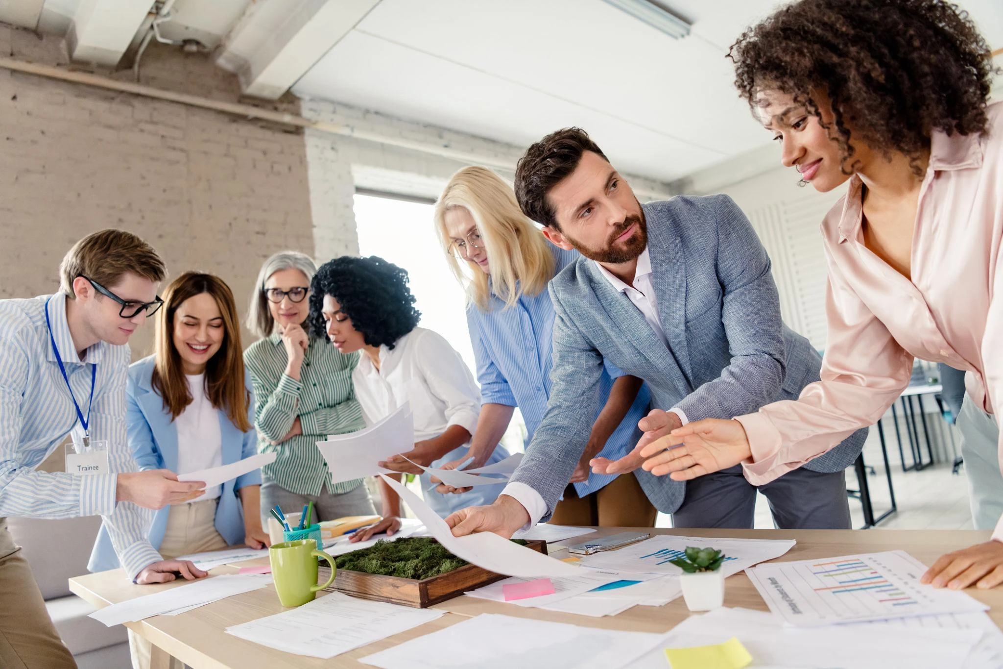 A group of professionals collaborates around a table, reviewing documents and discussing ideas in a modern office setting.