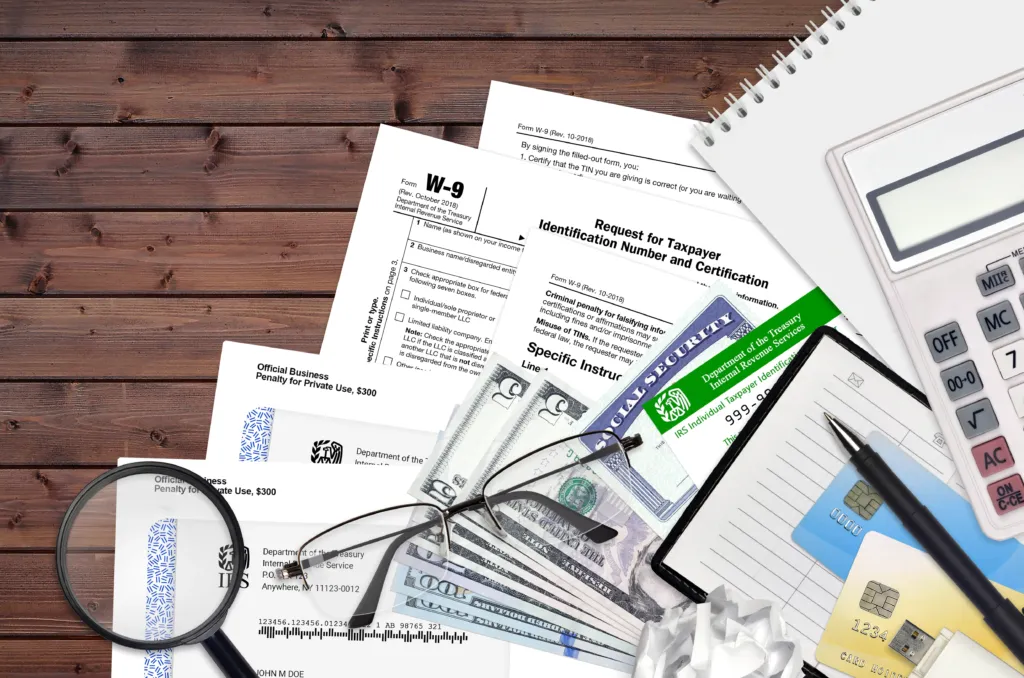 Assorted financial documents, money, credit cards, chequebook, magnifying glass, spectacles, and calculator on a wooden desk.