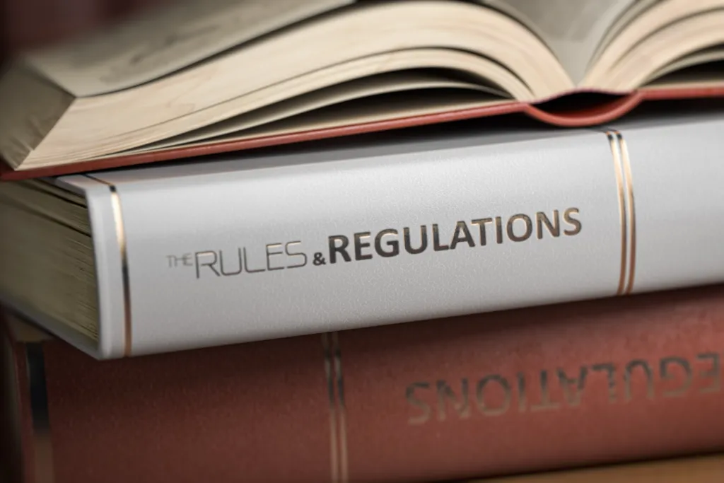 A binder labelled "Rules & Regulations" placed between other books, with an open book resting on top.