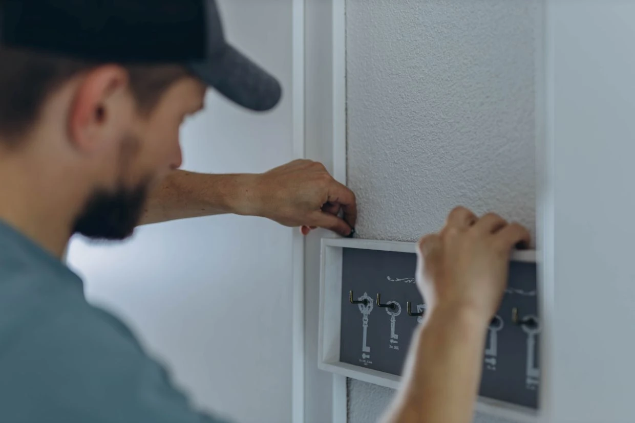 A person wearing a cap is adjusting controls on a wall-mounted panel with labelled levers or switches.