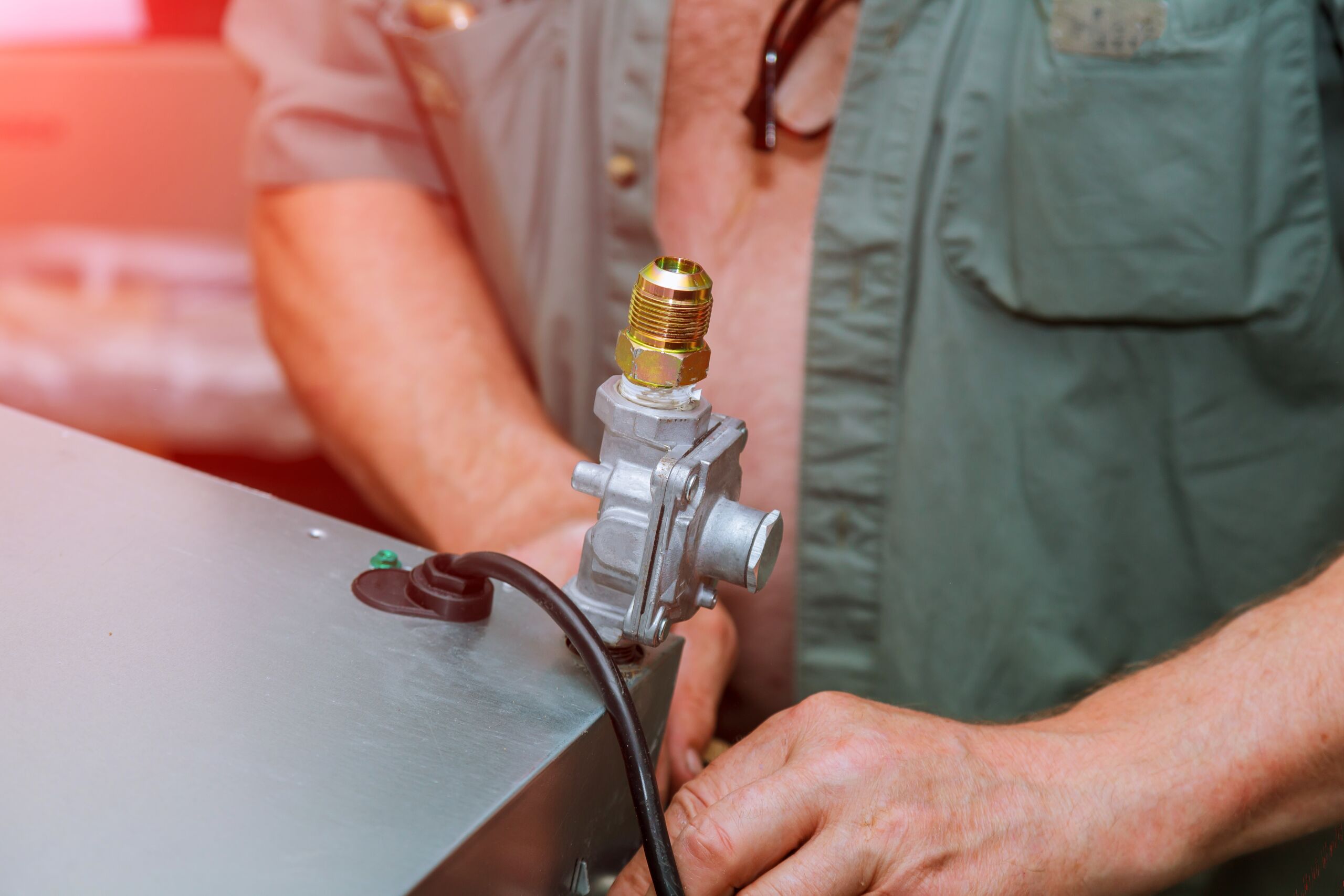 A person in a green shirt installs or repairs a gas valve on a metal appliance, with visible wires and fittings.