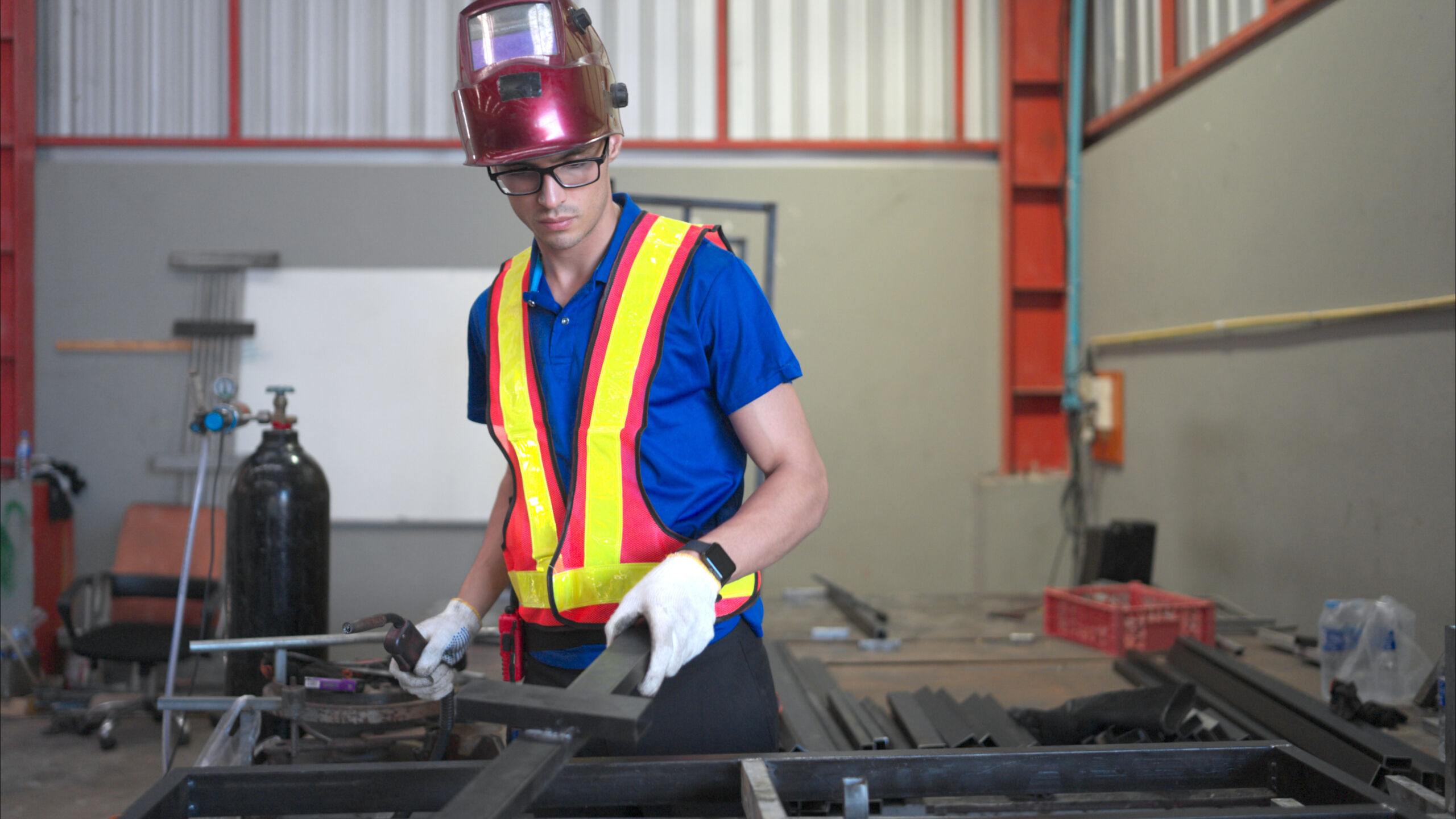 A worker in safety gear and a hard hat handles metal pieces in an industrial workshop.
